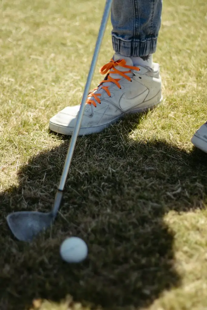 Golfer wear best golf shoes hold golf club on the course near golf ball 